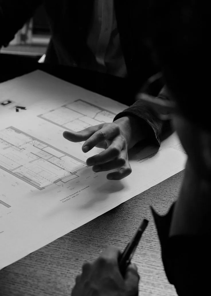 Hands pointing across architectural floor plans spread on a desk