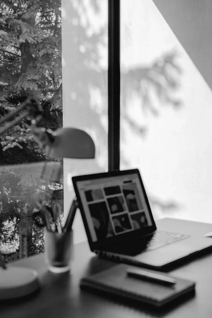 Sunlit studio desk with laptop and lamp behind a frosted window — the IN Investments Estate workspace